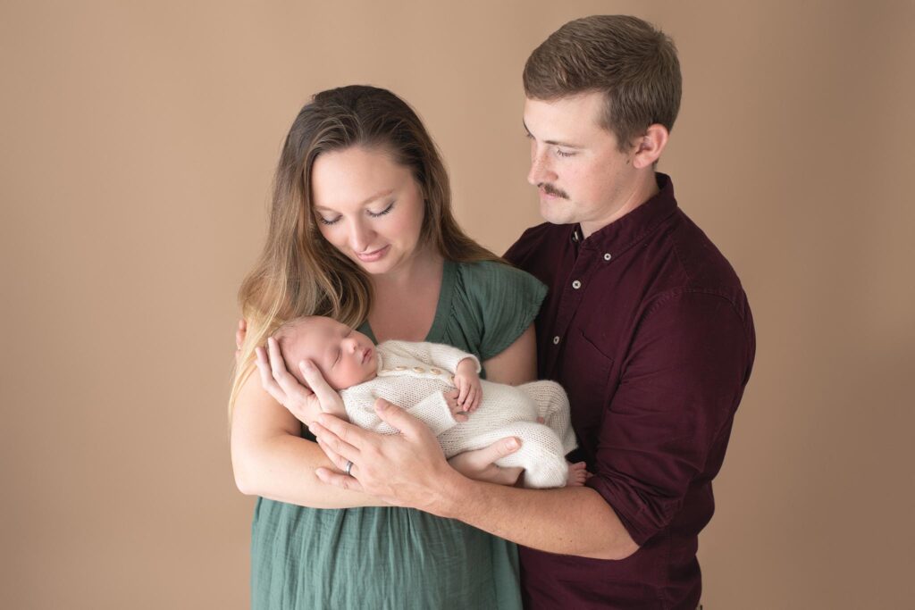 Mom, dad, and newborn baby on tan backdrop